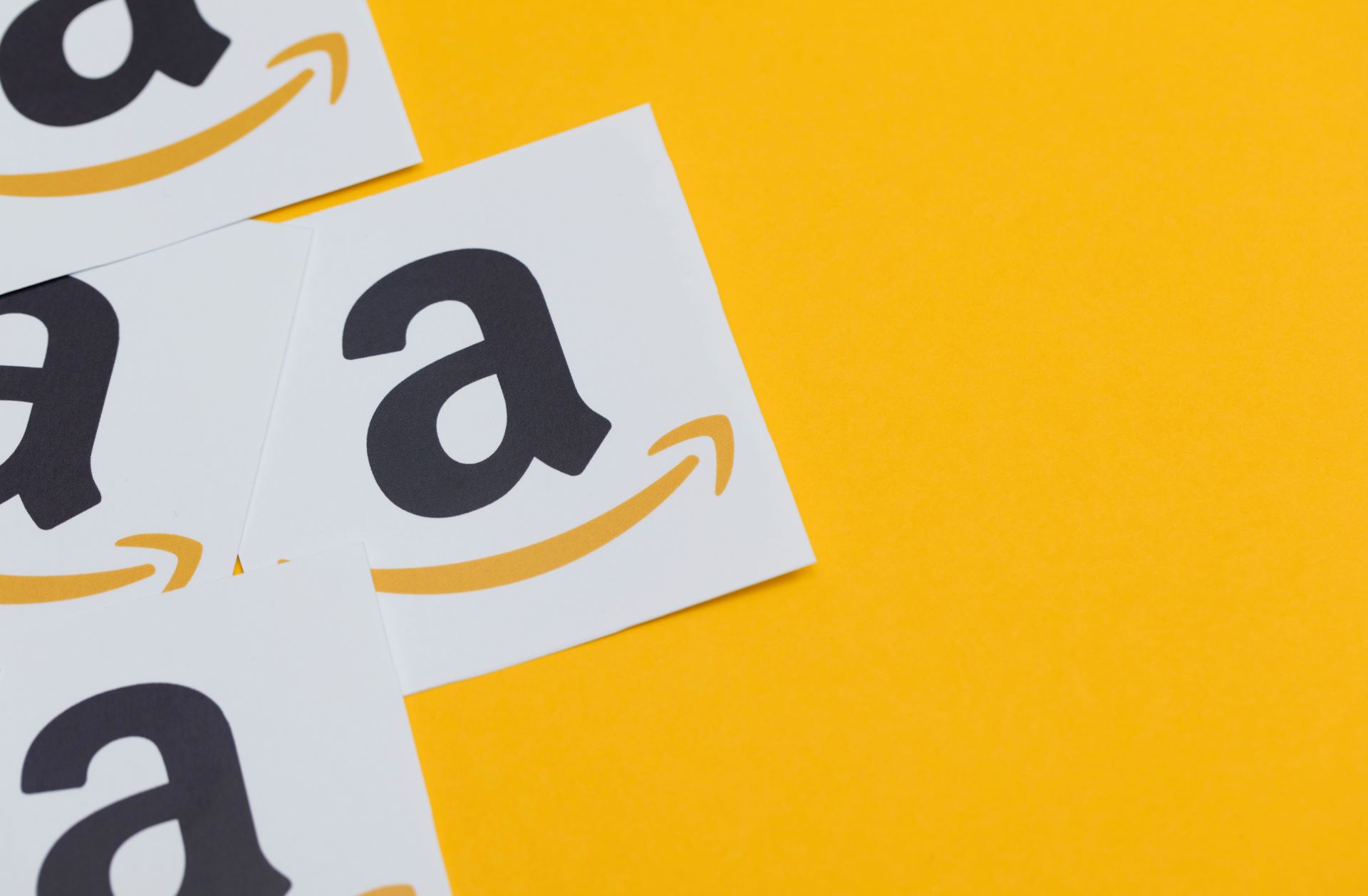 Mehrere Amazon-Logos auf weißem Hintergrund mit gelbem Untergrund, die das Branding von Amazon symbolisieren.